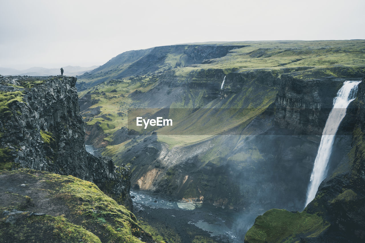 View of person standing on rocky mountain and waterfall