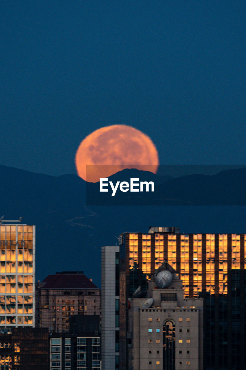 Illuminated buildings against moon in sky at night