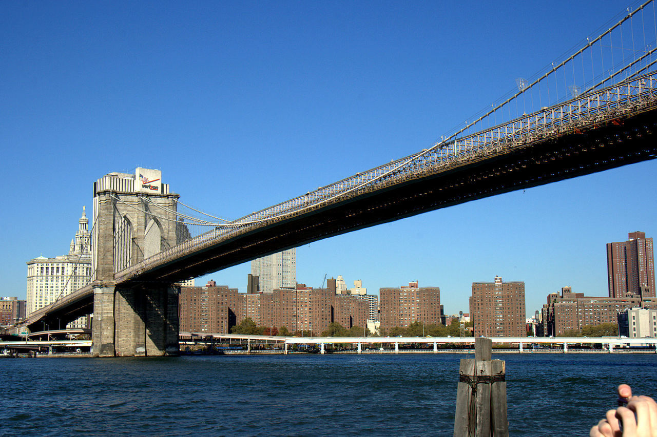 Low angle view of brooklyn bridge over east river against clear blue sky