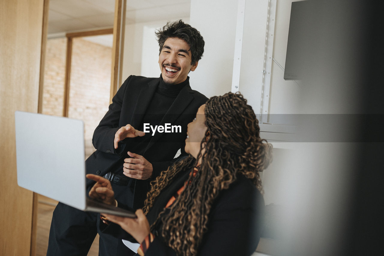 Female entrepreneur showing laptop to happy businessman at office