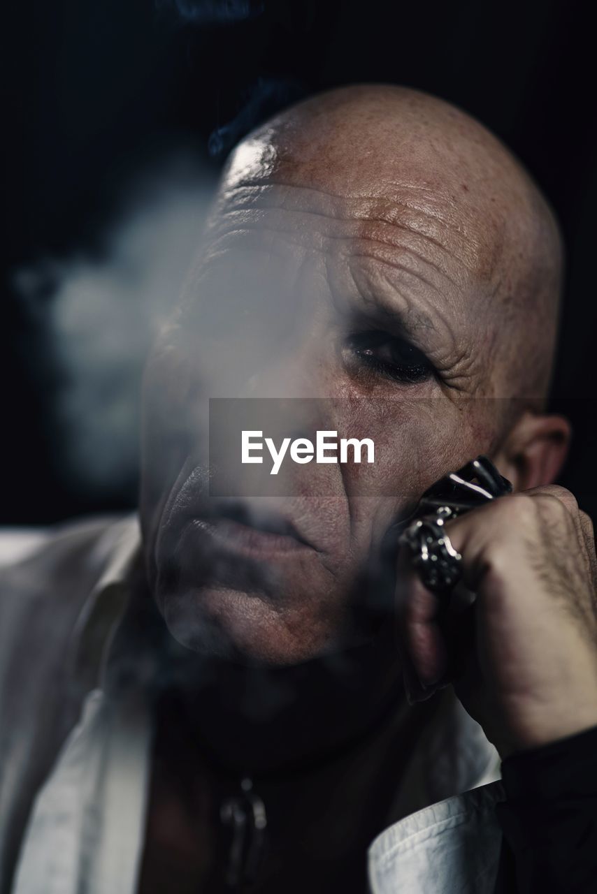 Close-up portrait of bald man smoking cigarette