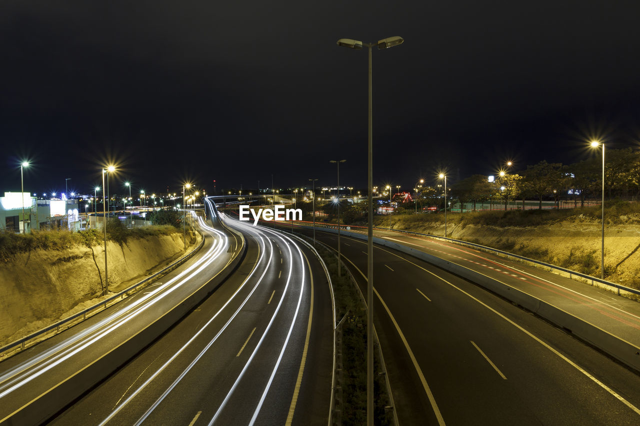 VIEW OF LIGHT TRAILS ON HIGHWAY AT NIGHT