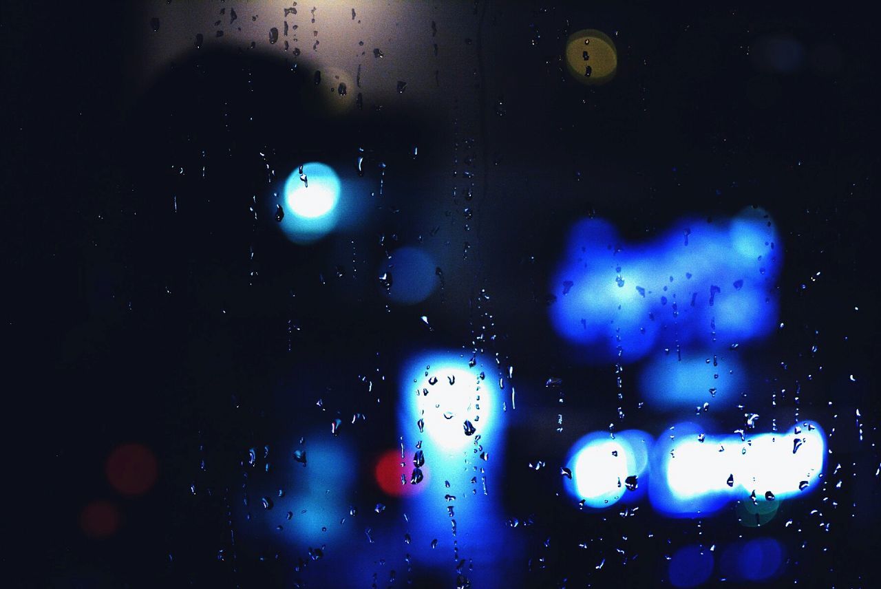 Close-up of wet window against illuminated lights at night