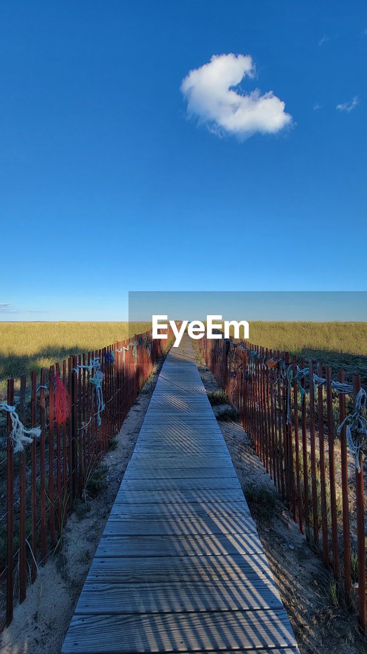 BOARDWALK AMIDST FIELD AGAINST SKY