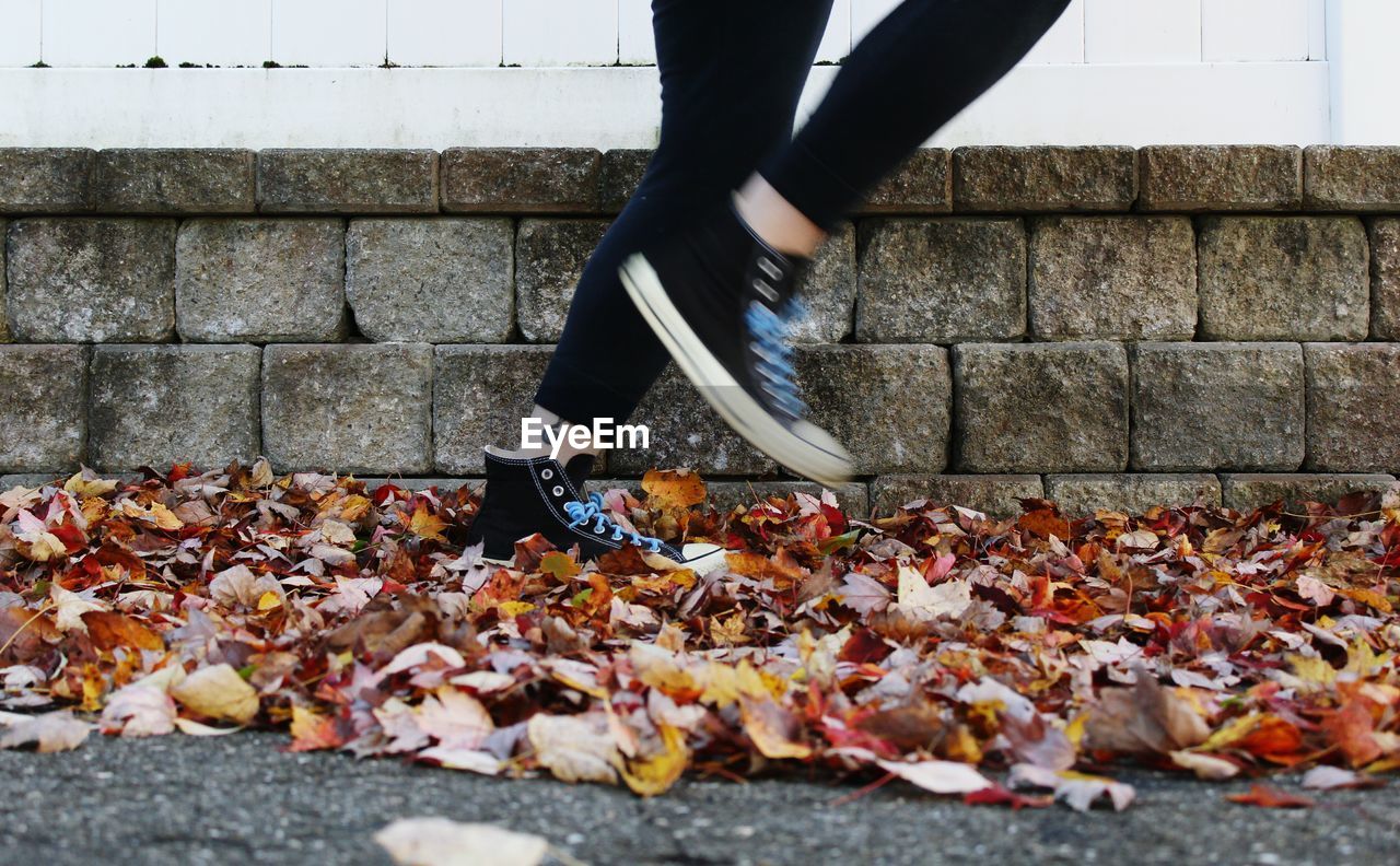 Low section of woman running on dry leaves