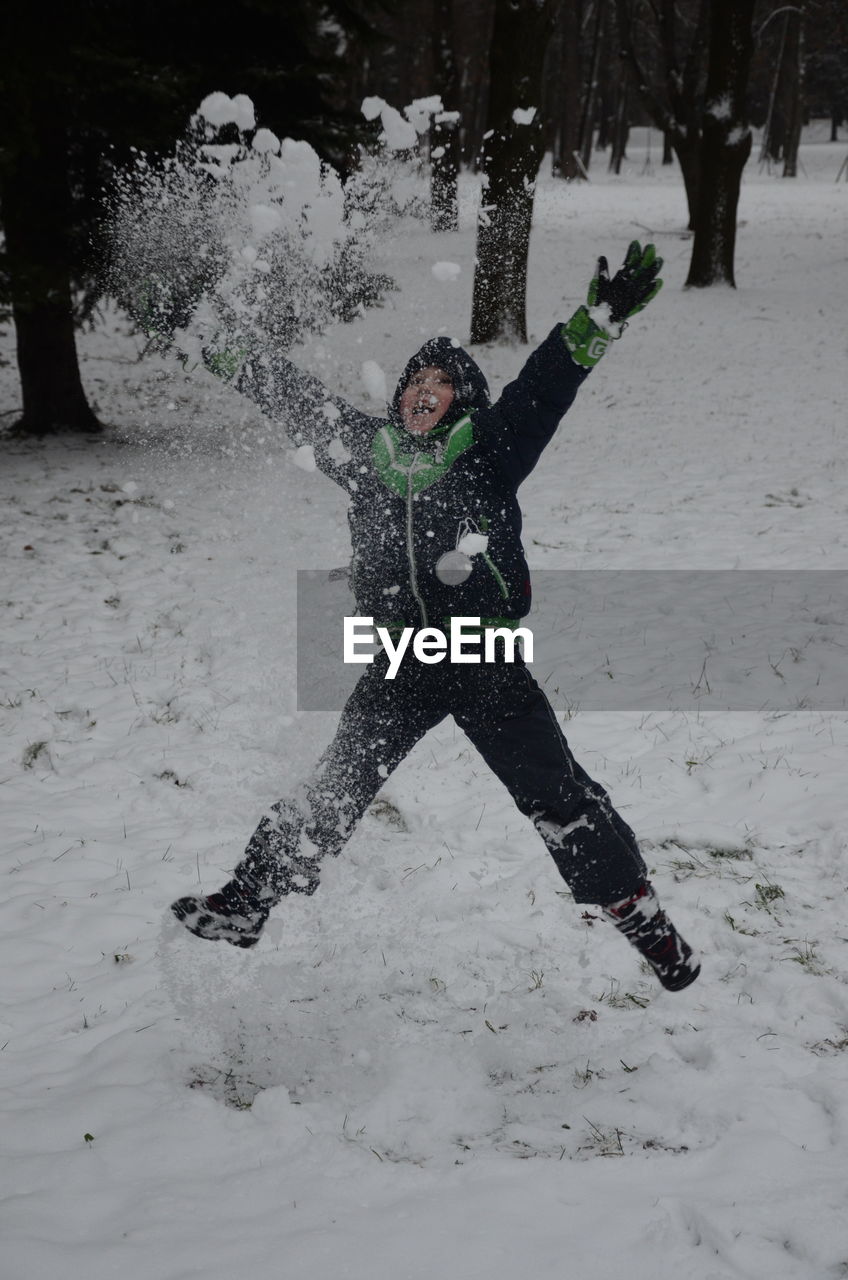 Cheerful boy throwing snow during winter