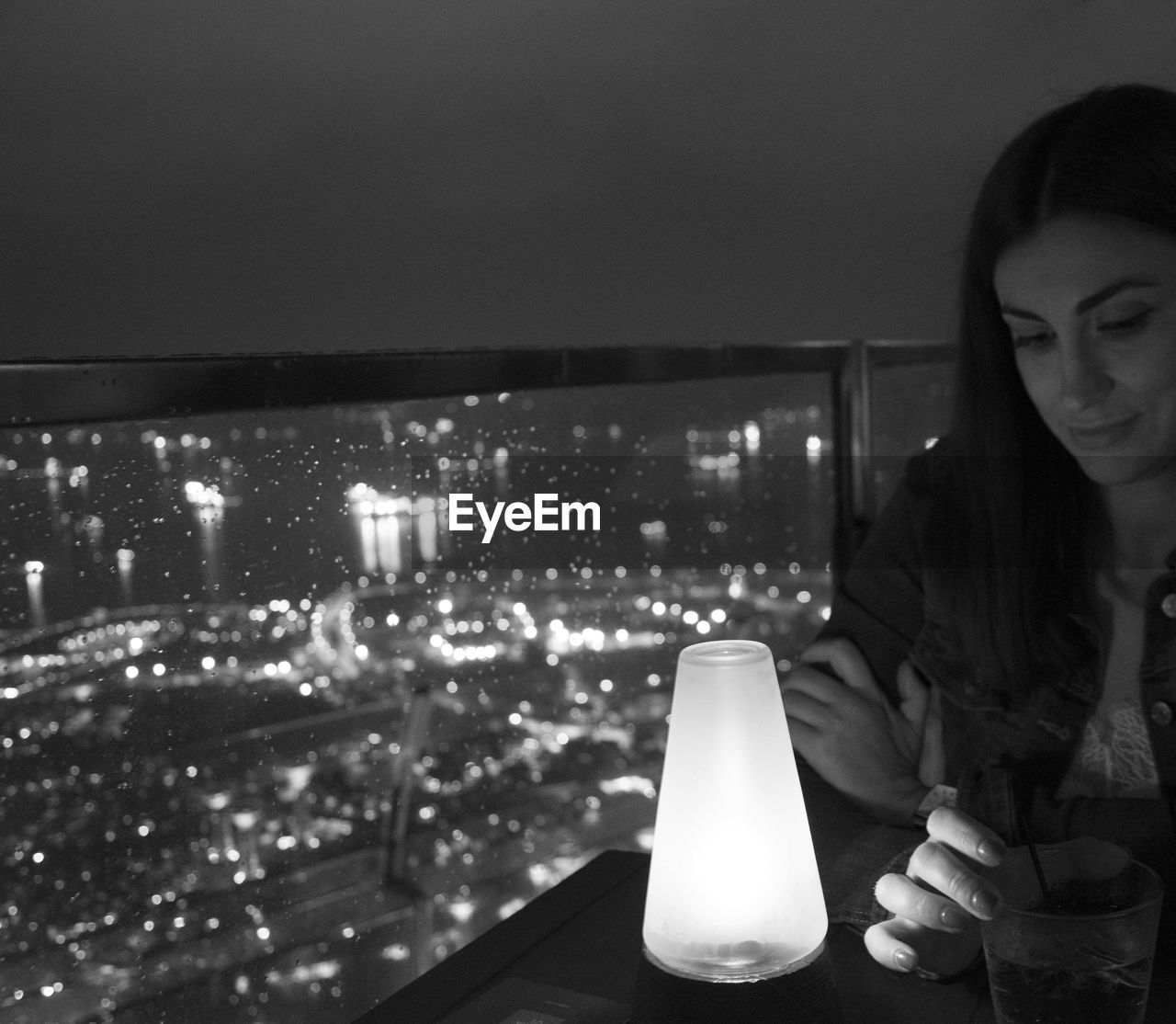 Mid adult woman with illuminated light sitting in restaurant against sky at night