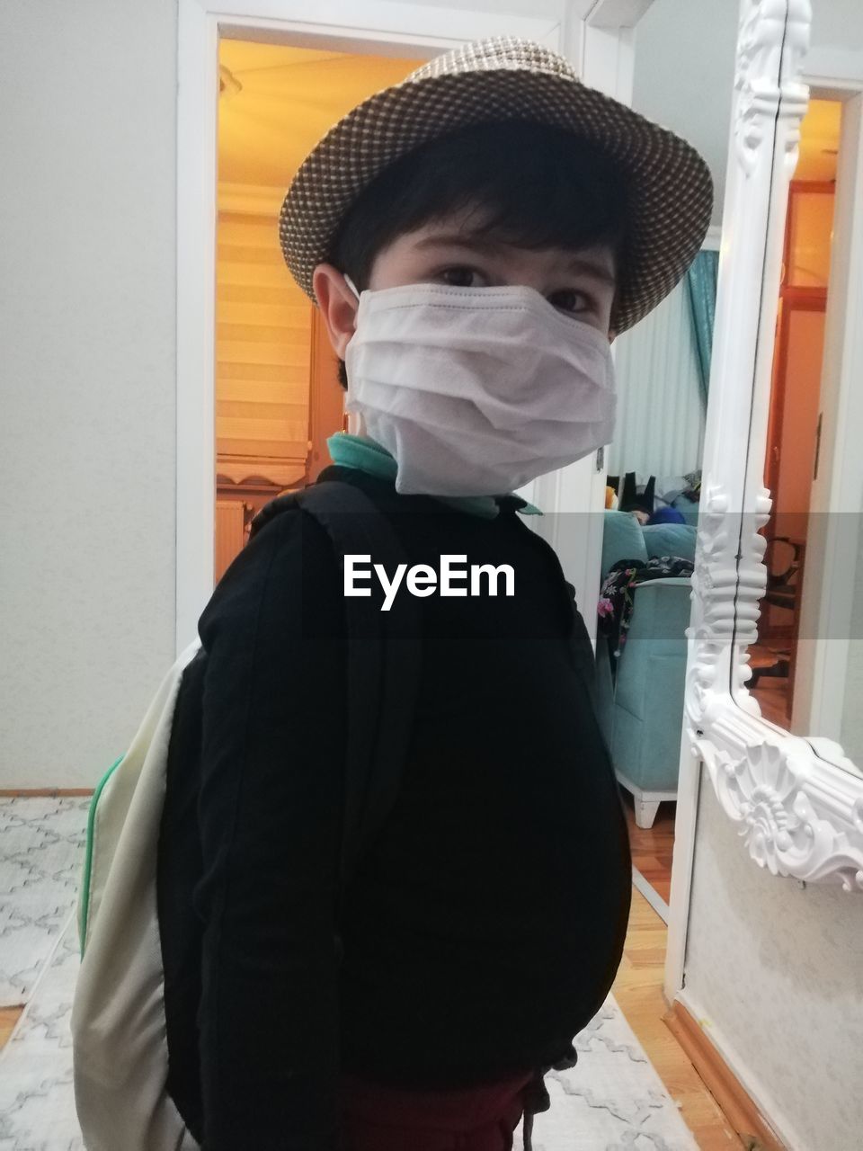 Portrait of boy wearing mask and hat standing at home
