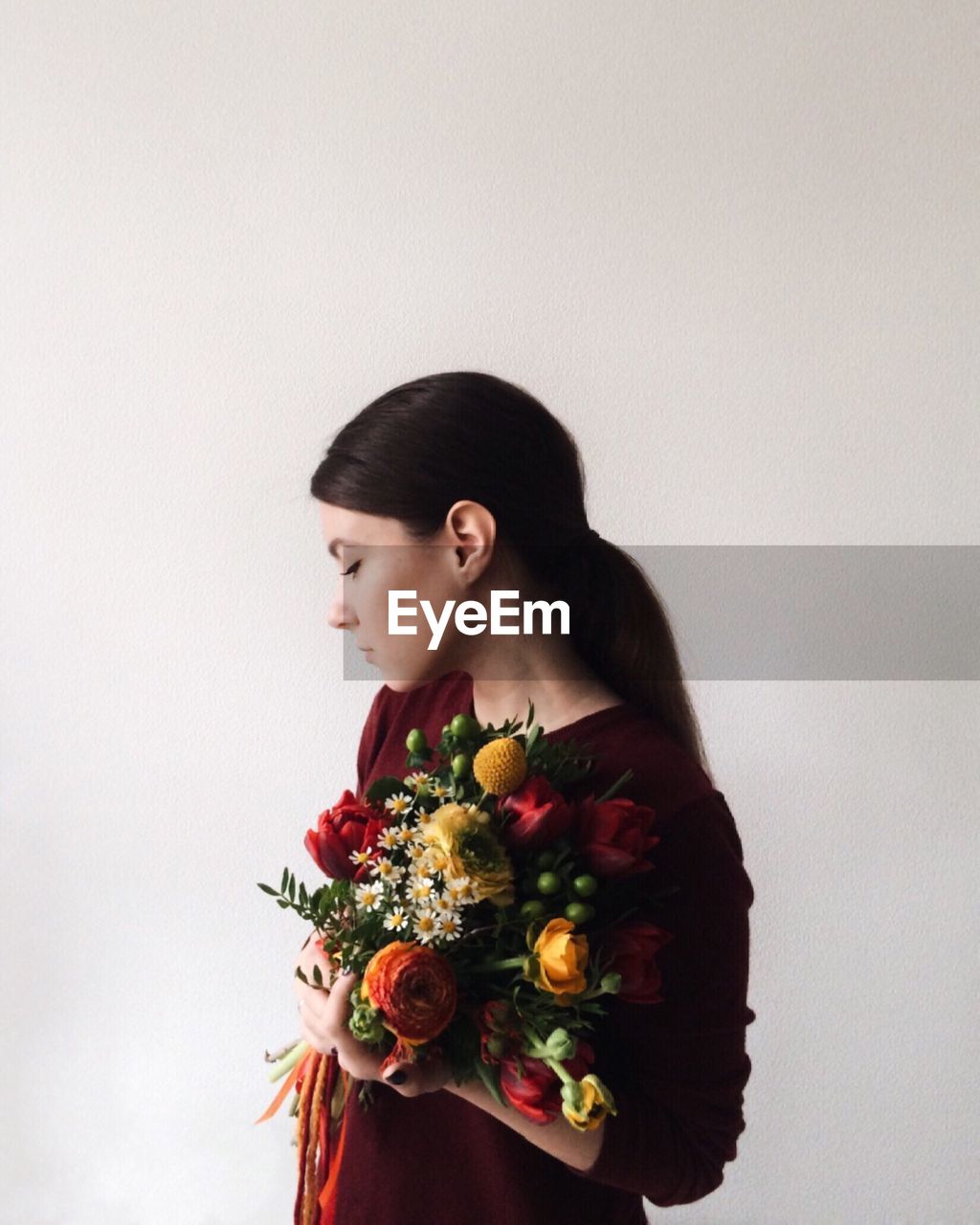 Woman holding bouquet while standing against white background