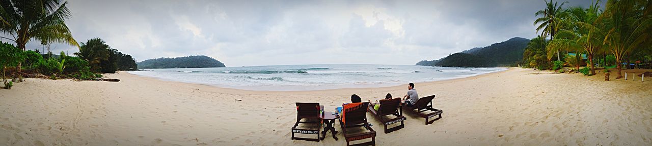 Panoramic view of people relaxing on deck chairs at beach