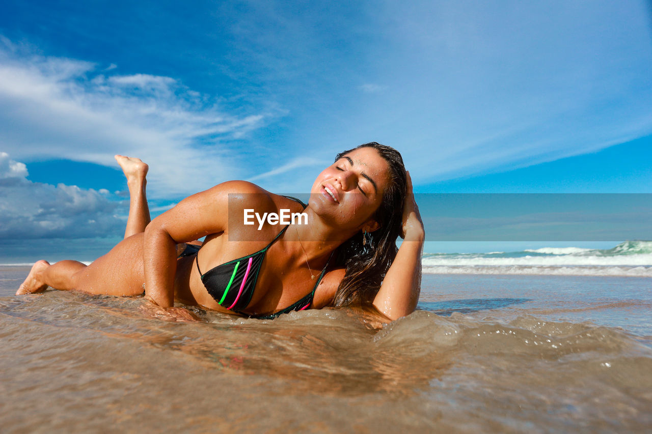 Young woman in bikini on beach against sky