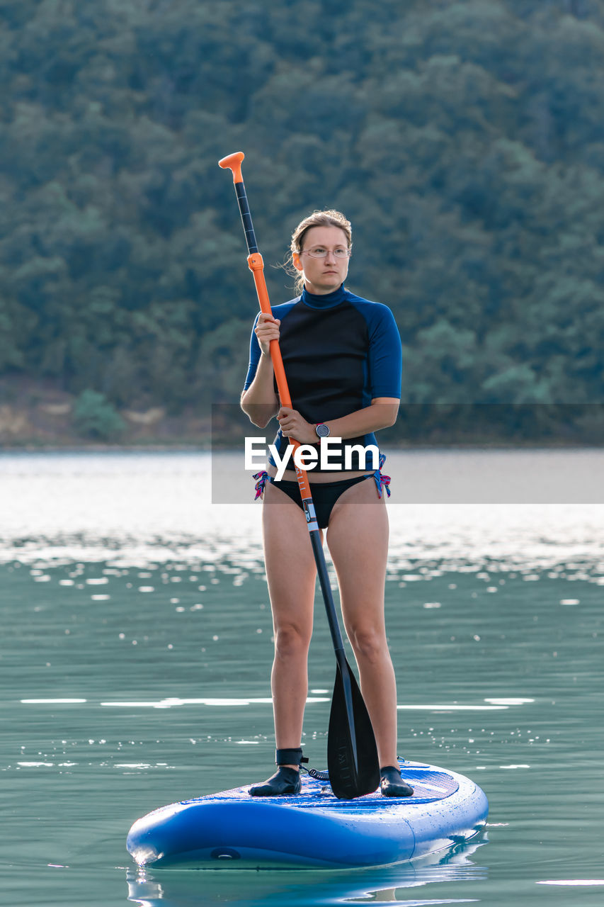 Full length of woman holding oar while standing on boat in sea