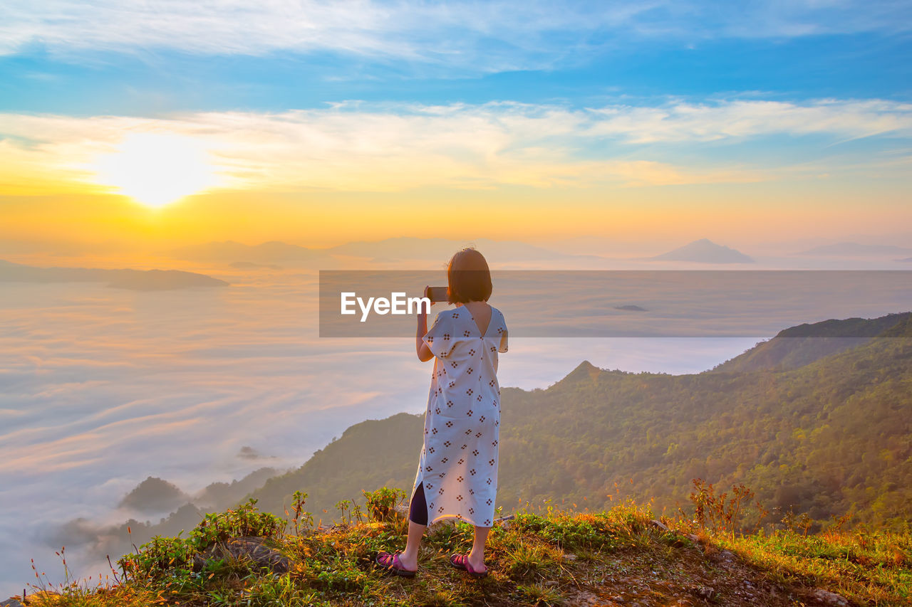 Woman photographing cloudscape during sunset