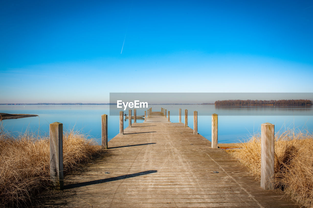 Wooden pier on sea against clear blue sky