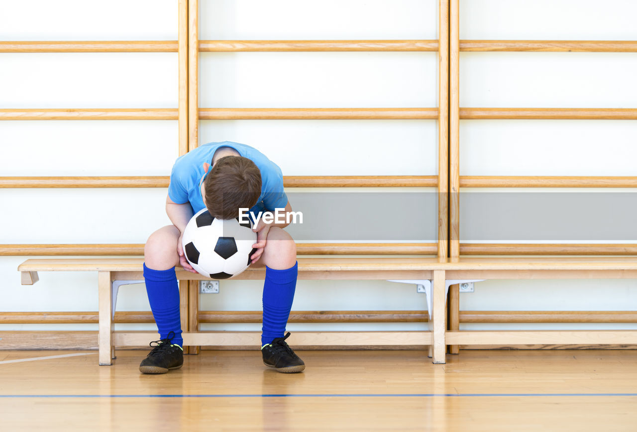 Boy with soccer ball sitting on bench