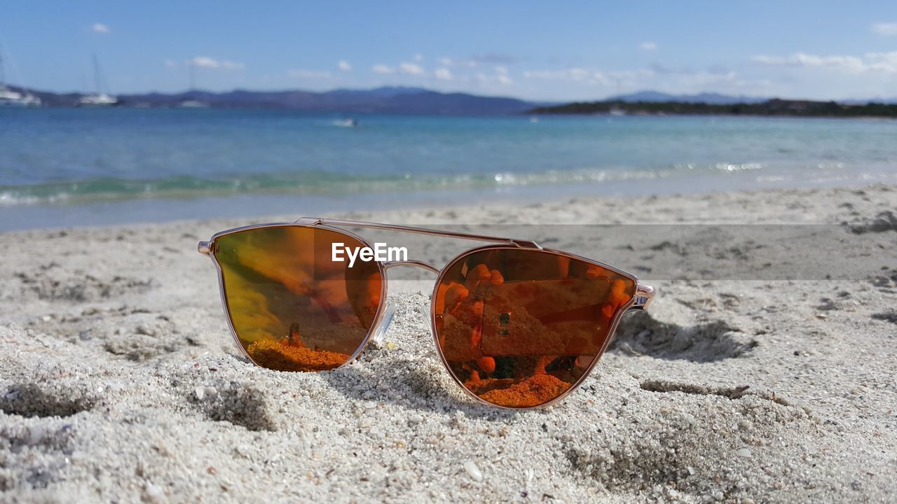 CLOSE-UP OF SUNGLASSES ON SAND AT BEACH