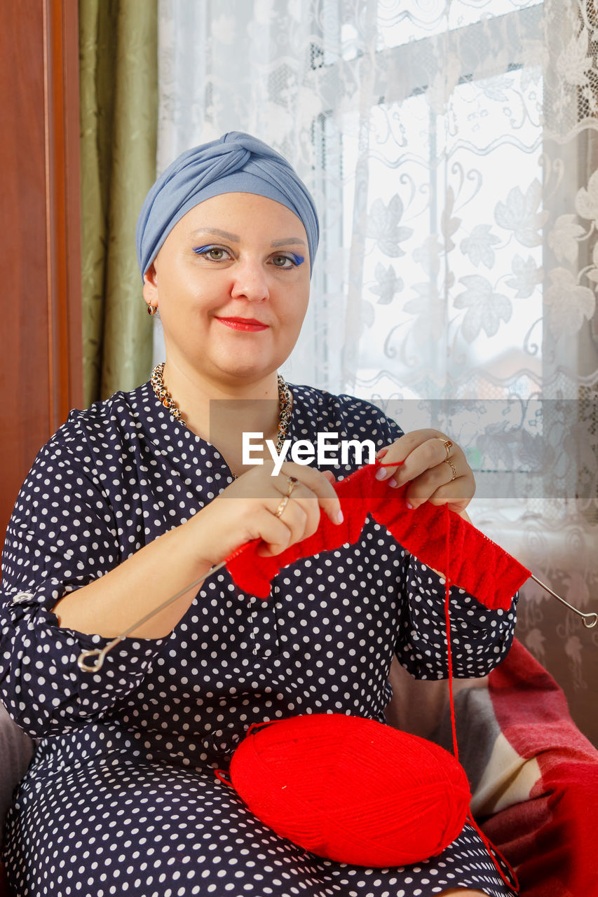 one person, women, adult, polka dot, indoors, portrait, red, looking at camera, clothing, young adult, pattern, headscarf, female, lifestyles, front view, smiling, holding, sitting, waist up, fashion, emotion, photo shoot, happiness, spotted, dress, person, curtain, domestic room, leisure activity, home interior