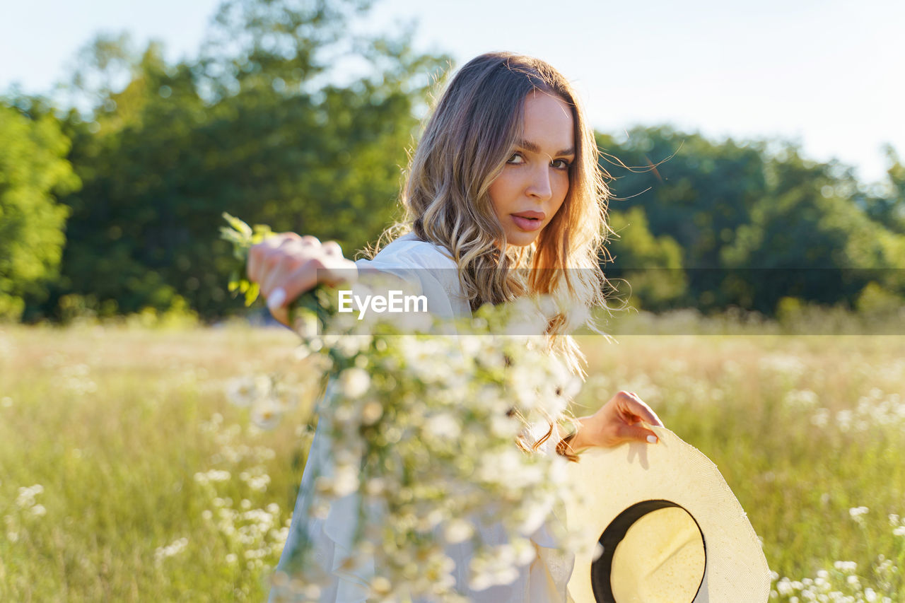 PORTRAIT OF WOMAN WITH FLOWERS ON FIELD IN BACKGROUND