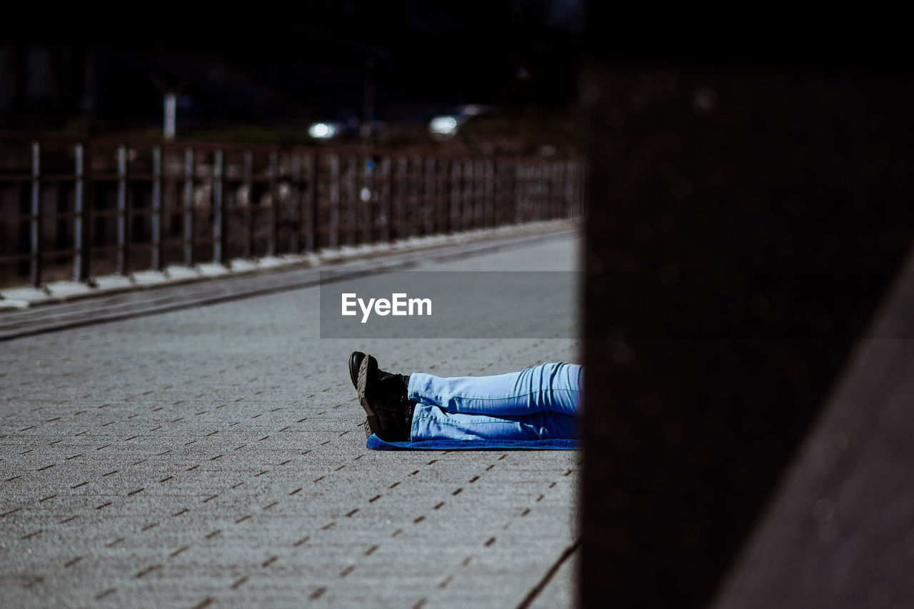 Low section of man relaxing on footpath during sunny day