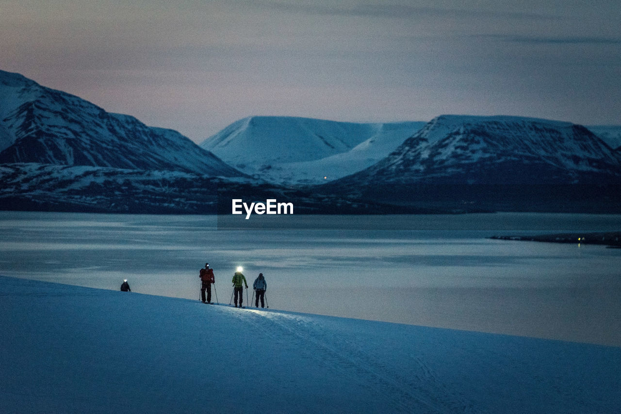 A group of 3 people skis at sunrise with ocean and mountains behind