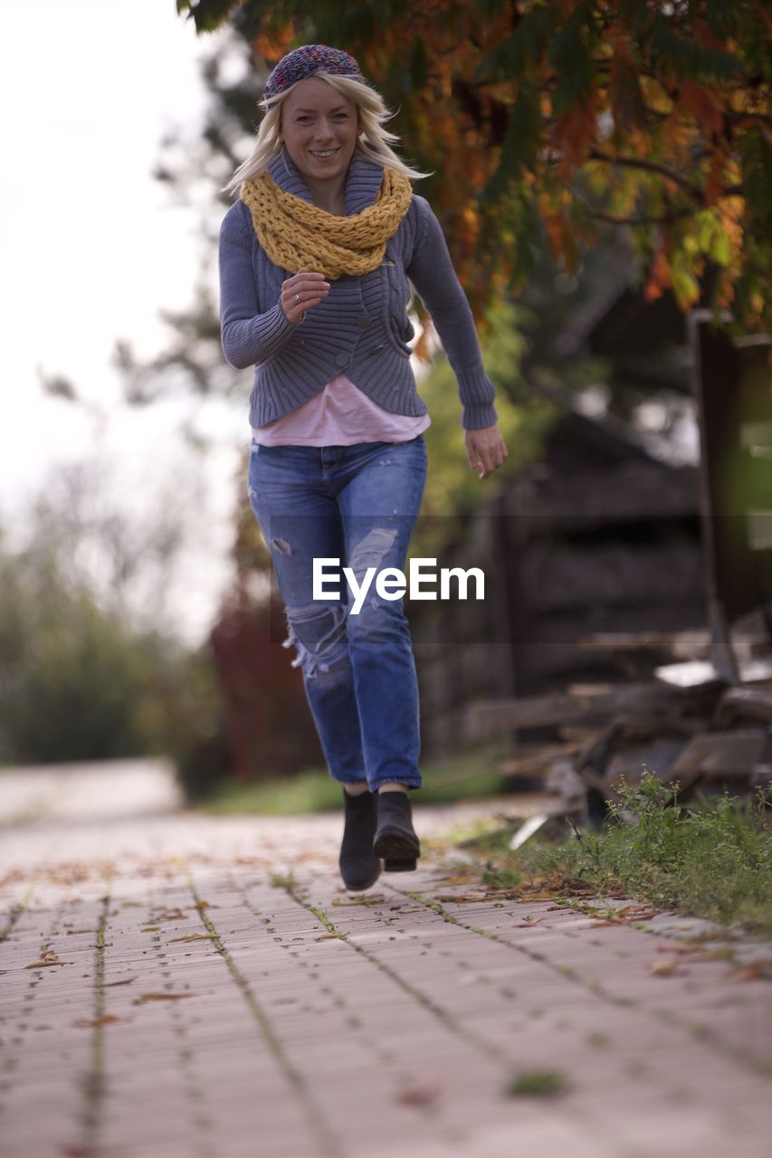 Blonde woman smiling dressed in wool sweater beret and wool scarf on fall run