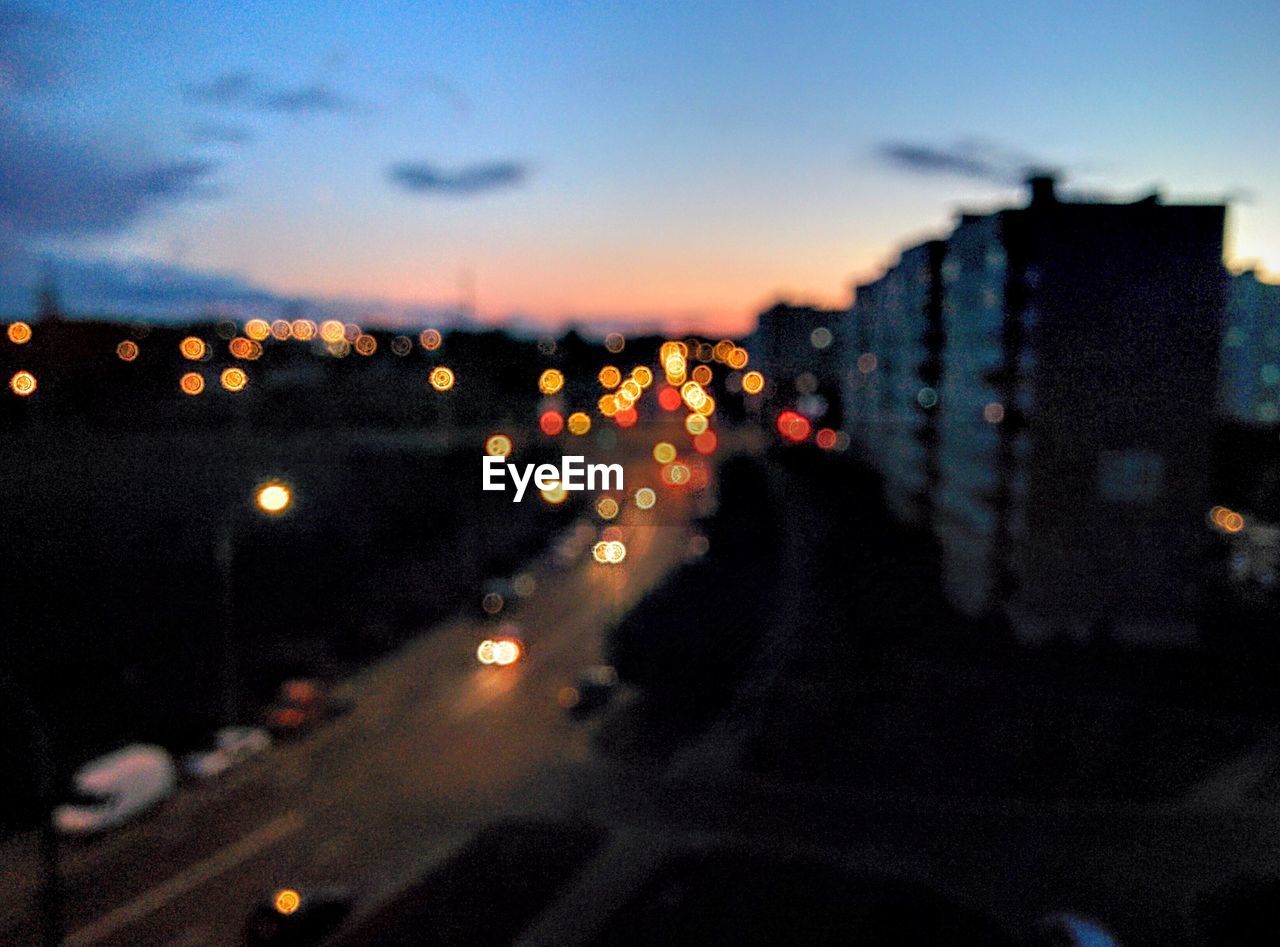 Defocused image of illuminated cityscape against blue sky