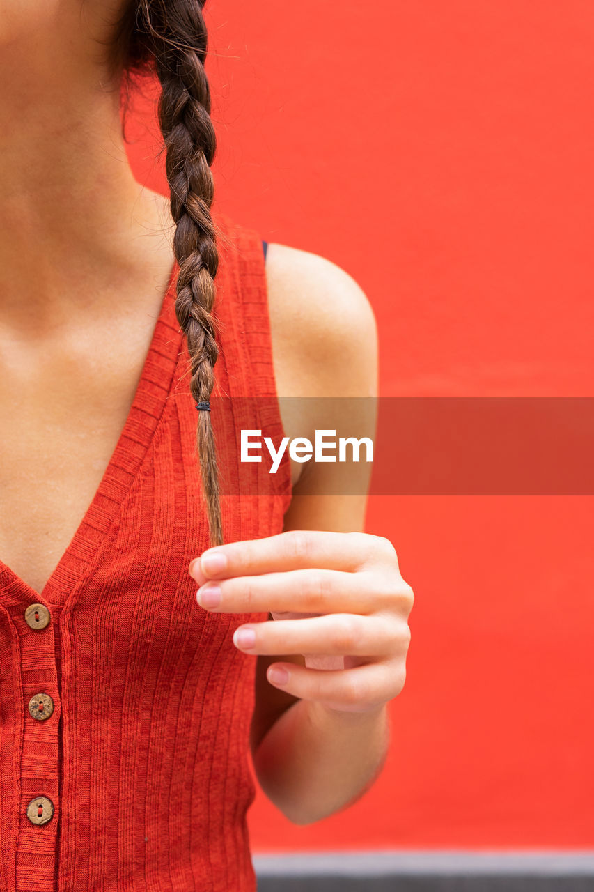 Crop young female touching pigtails on red background in street