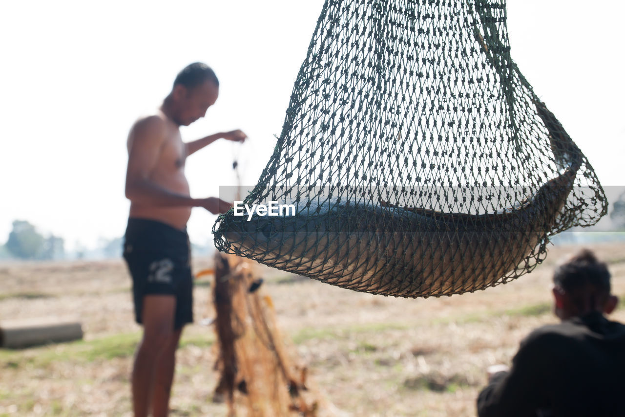 Close-up of fish in net against men on field