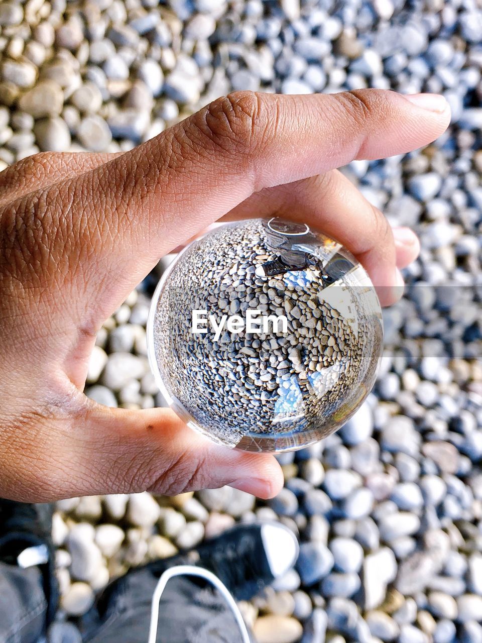 Low section of man holding crystal ball over pebbles