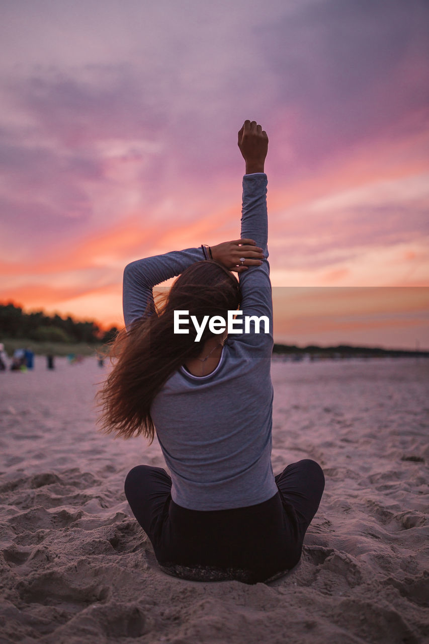 Rear view of woman doing yoga at beach during sunrise
