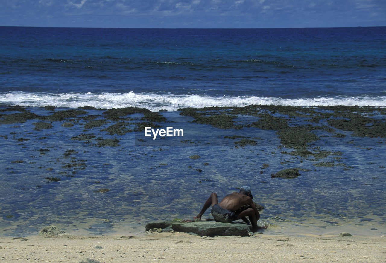 Rear view of fisherman sitting on beach during sunny day