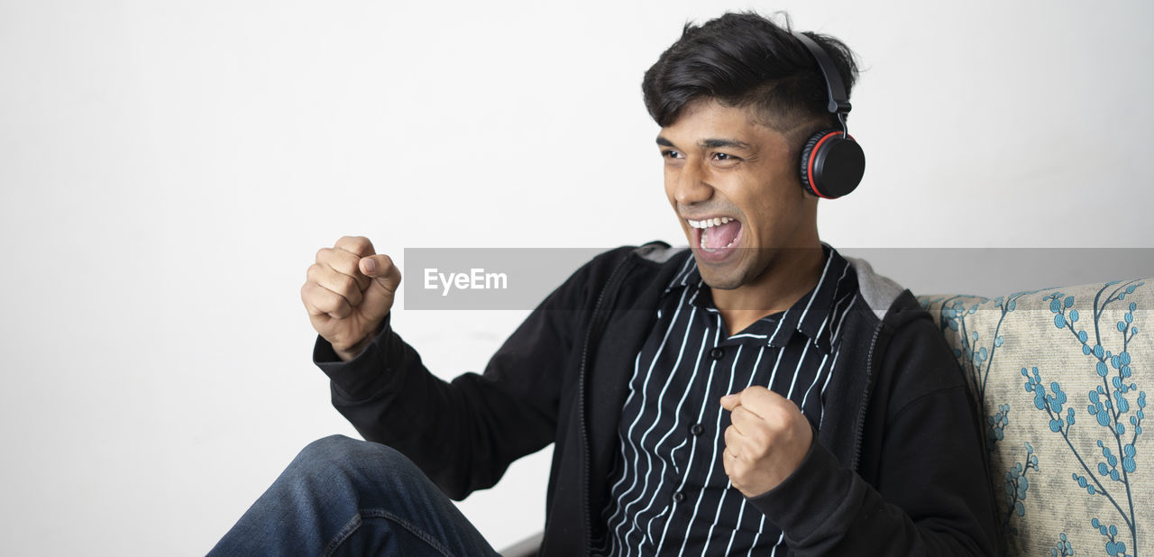 Asian man with headphone while wearing black jacket positive gesture with hand, smiling.