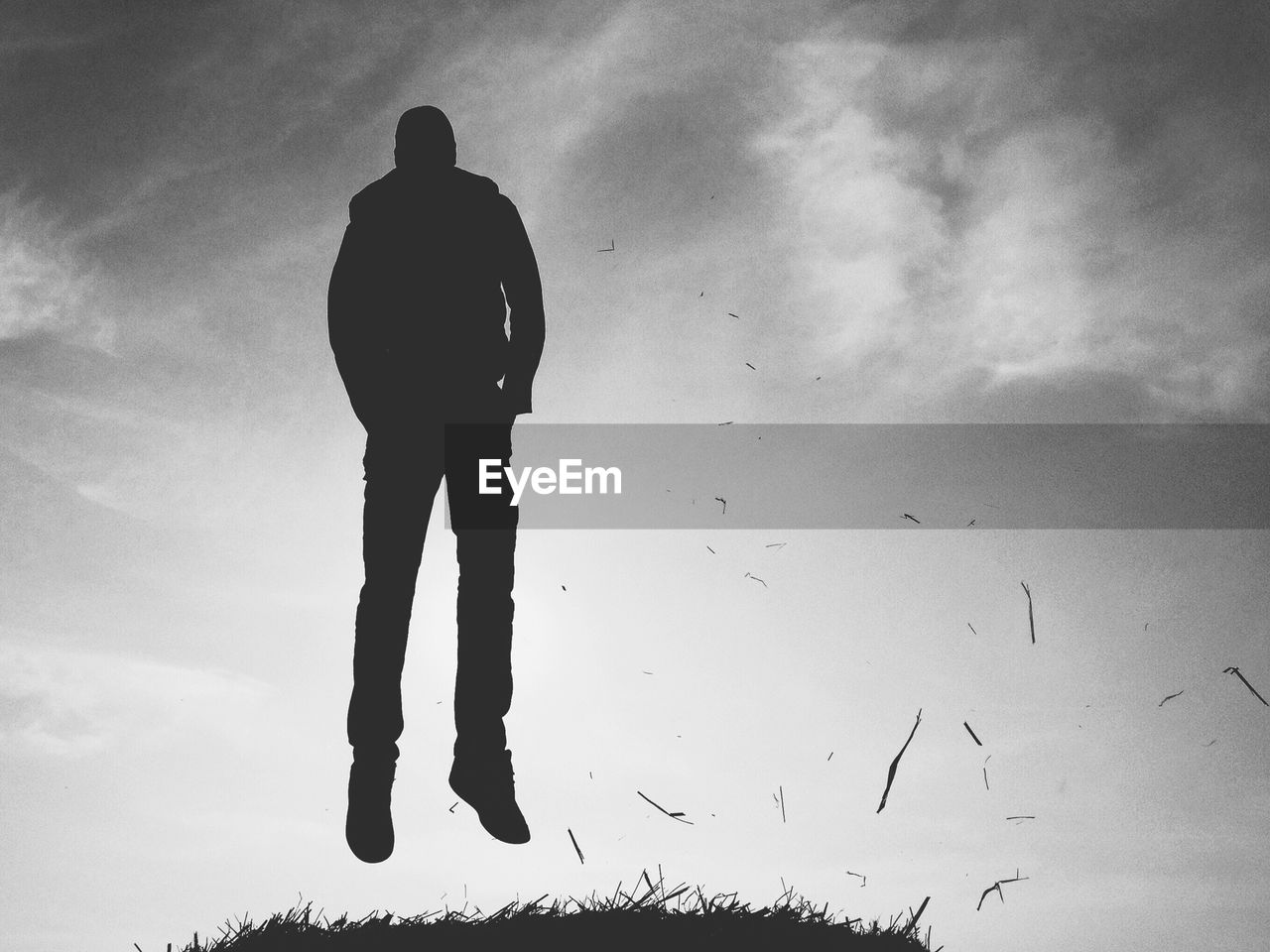 Silhouette man levitating above grass against sky