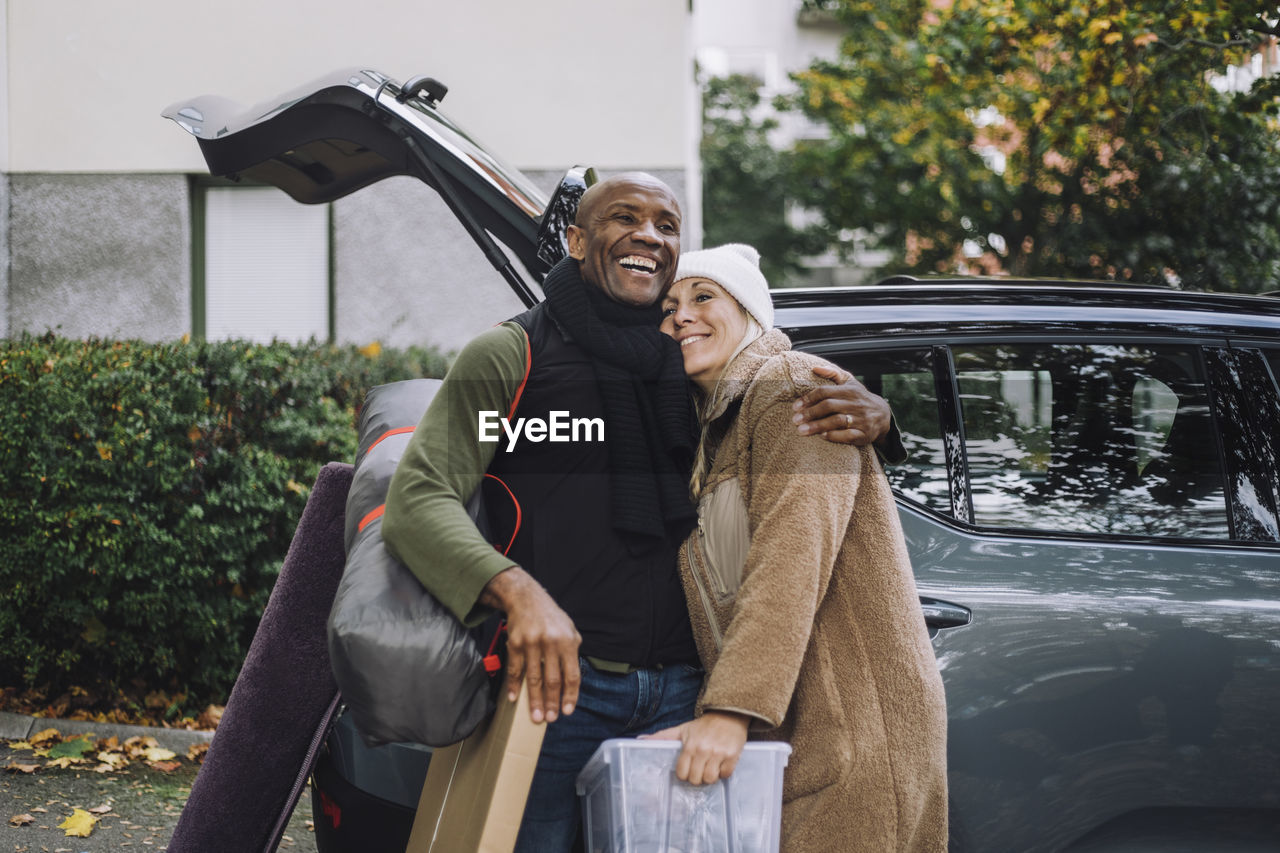 Happy mature man embracing woman while standing near car