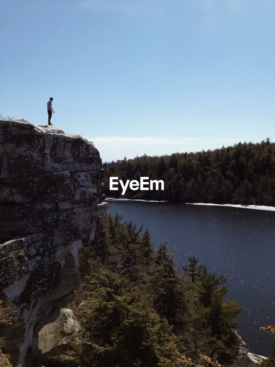 Man standing on cliff by lake against clear sky