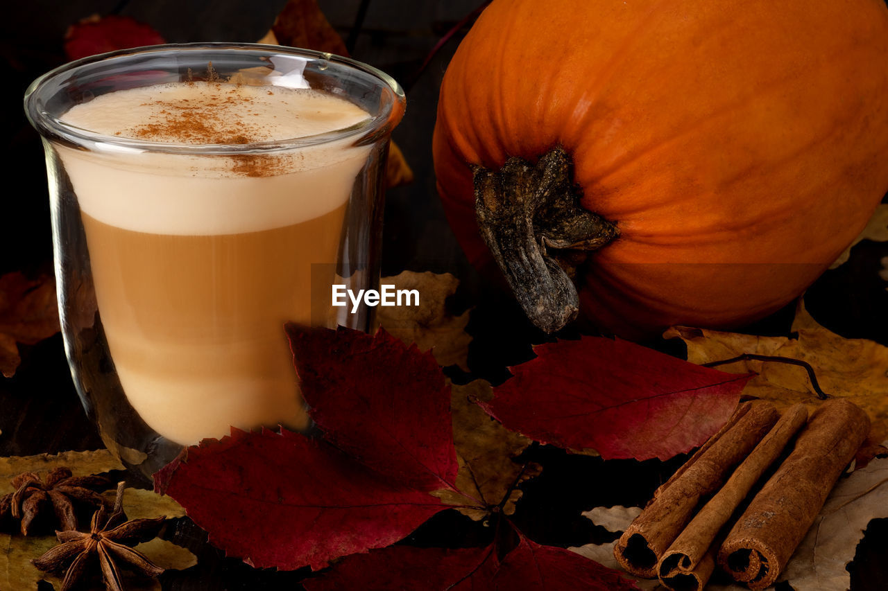 Glass cup with latte and pumpkin stand on a stand with autumn leaves. autumn hygge concept. 