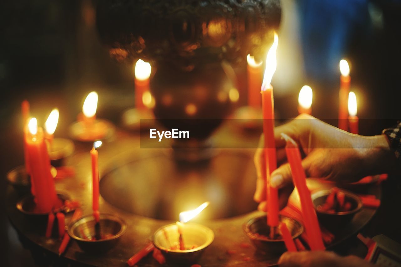 Cropped hand of woman burning candles in temple