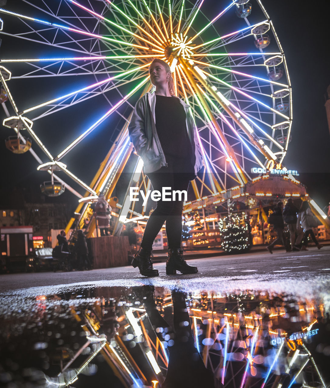 Woman standing against illuminated ferris wheel at night