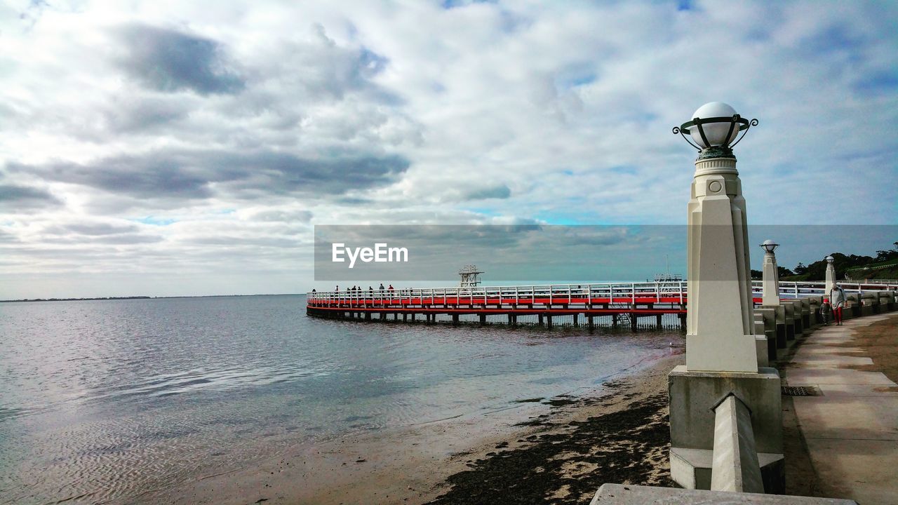 Footpath by sea against cloudy sky