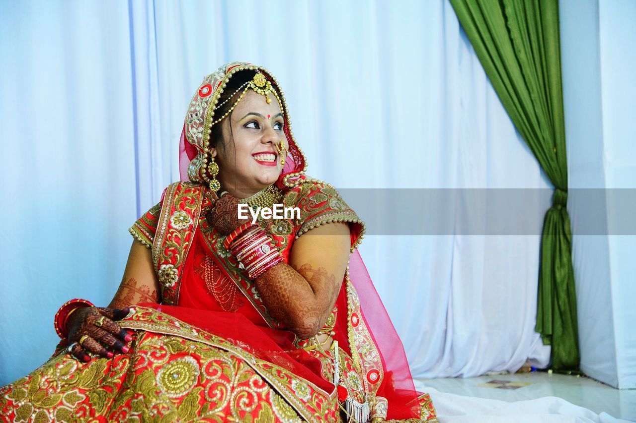 Close-up of bride sitting on chair against curtains