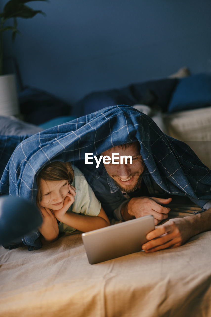 Happy father and son watching a movie on tablet under blanket