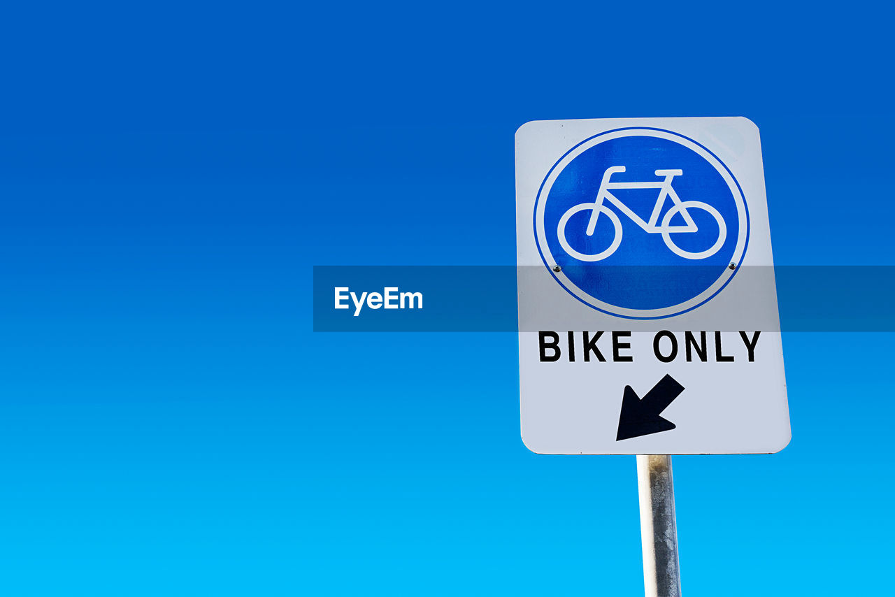 Low angle view of road sign against clear blue sky