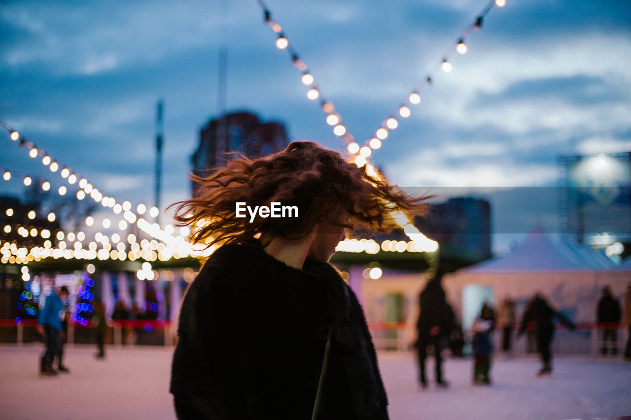 Woman shaking head against illuminated lights at dusk