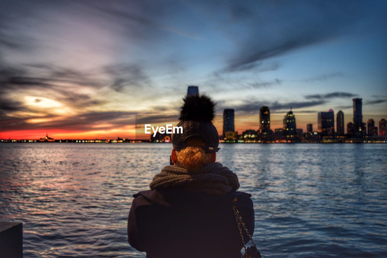 Rear view of a man overlooking river with buildings in distance