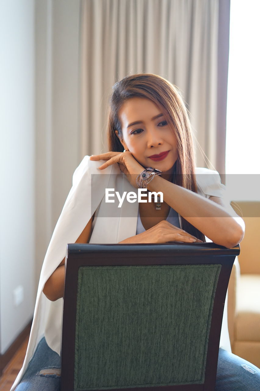 Thoughtful woman sitting on chair at home