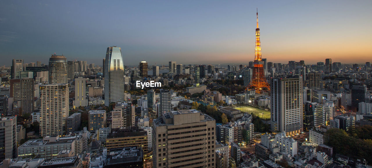 Illuminated tokyo tower in city against clear sky during sunset