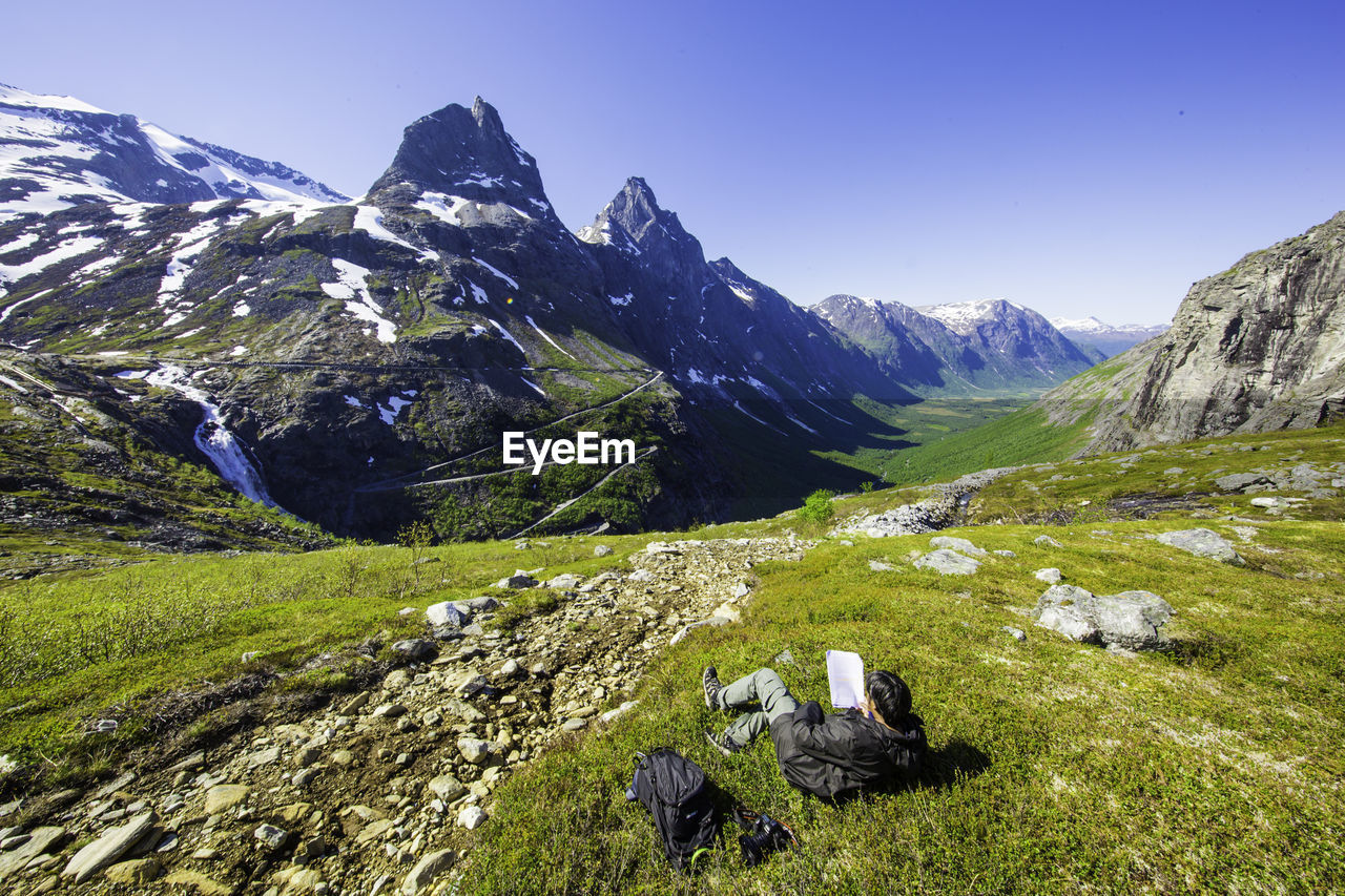 Rear view full length of man lying down on grassy field against mountain