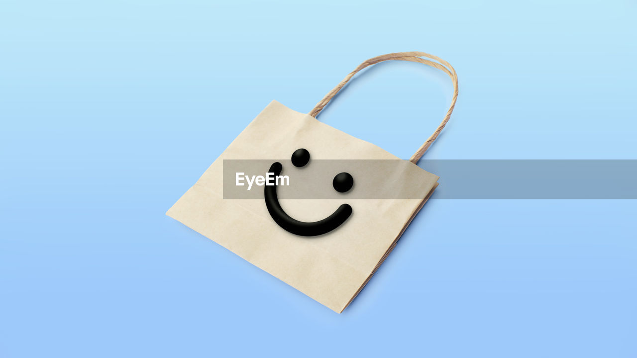 Smile face on kraft paper bag with handles isolated on blue background. shopping packaging.