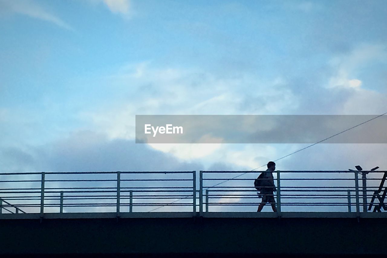 Low angle view of man walking on footbridge against sky