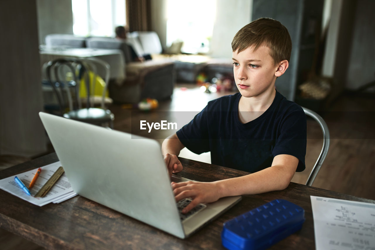 REAR VIEW OF BOY SITTING AT TABLE